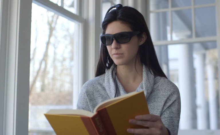 A woman wearing dark cool gadgets 2019 glasses and reading a book.