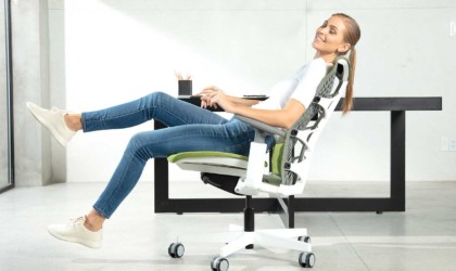 A woman is sitting in an office chair, slightly tilted back and smiling.