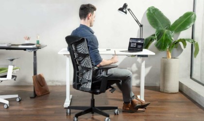 A man is sitting in a black office chair and working at a laptop.
