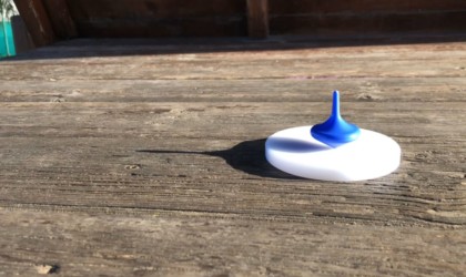 A white coaster with a blue latest tech gadgets spinning top on it, on a wood table.