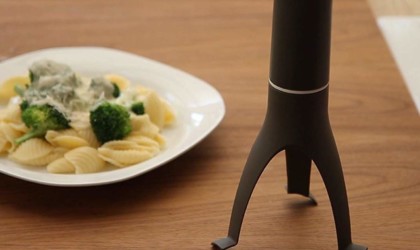 A self-stirring kitchen accessories and gadgets on a counter next to a plate of pasta.