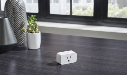 A smart plug is sitting on a dark wood table.
