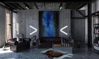A view of a modern industrial living space with touch lights in the shape of arrows on the wall, pointing toward a blue painting.