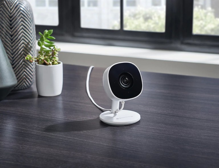 A small black and white home security cam is on a dark wood table.